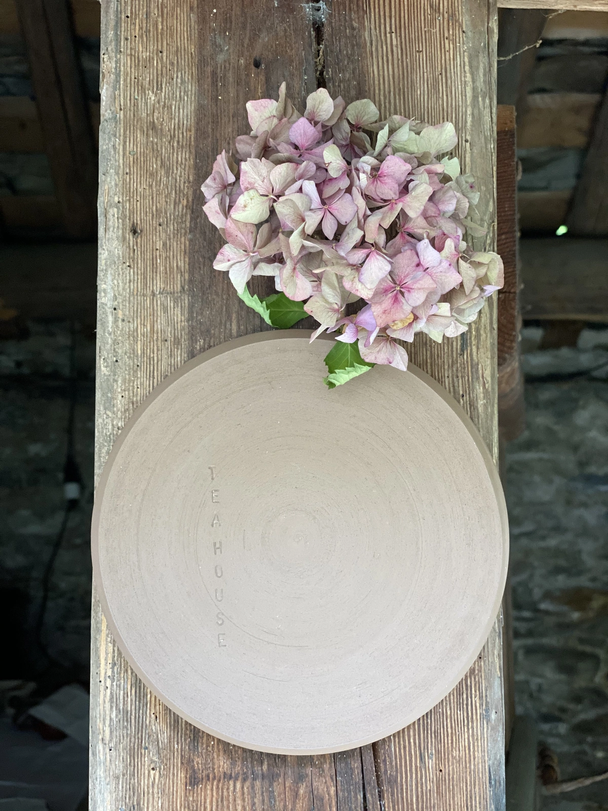 Round ceramic teahouse nameplate with dried pink hydrangea hung on the wooden doorframe.